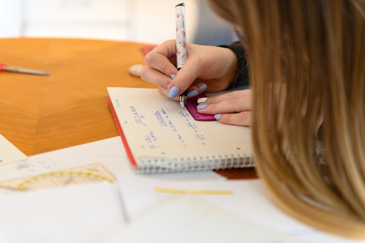 En ung flicka sitter vid en skolbänk och räknar mattetal i en skrivbok