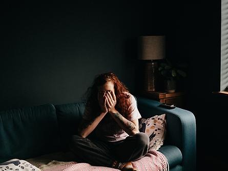 Girl sits on bed in darkened room, her face is in her hands.