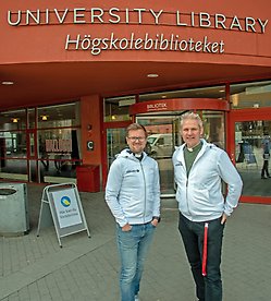 Two men in front of a red building 